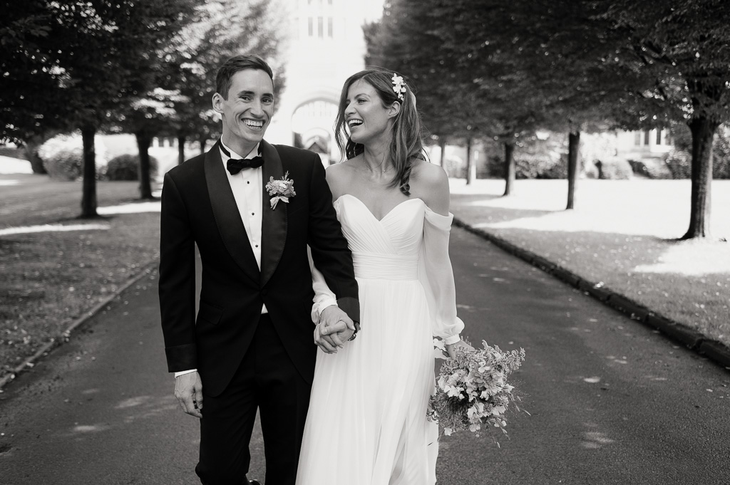 black and white photo of wedding couple walking holding hands and laughing